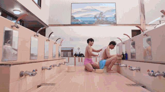 two men are taking a shower in a bathroom with a painting on the wall