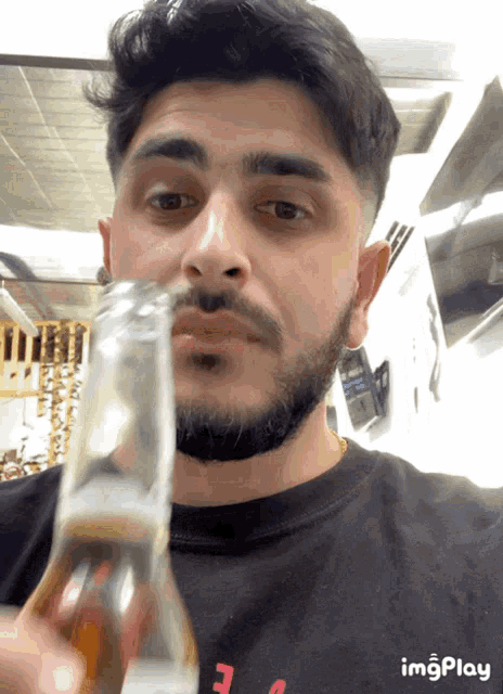 a man with a beard is drinking from a bottle with a black shirt that says imgplay