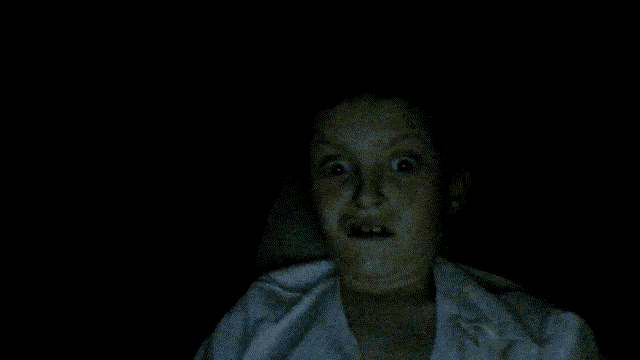 a person with their mouth open in the dark with a white shirt on