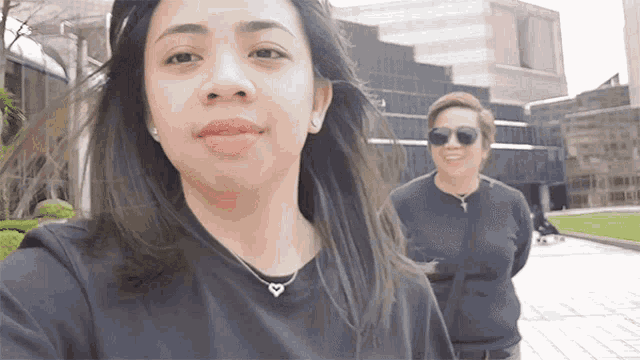 a woman wearing sunglasses and a heart necklace is standing next to another woman
