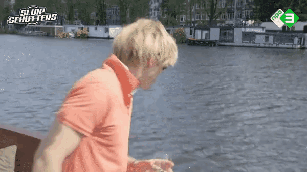 a man in an orange shirt stands in front of a body of water with a npo tv logo in the background