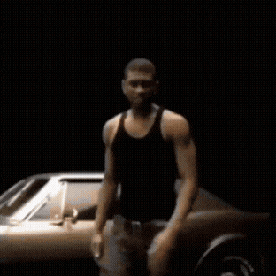 a man in a black tank top stands in front of a silver car