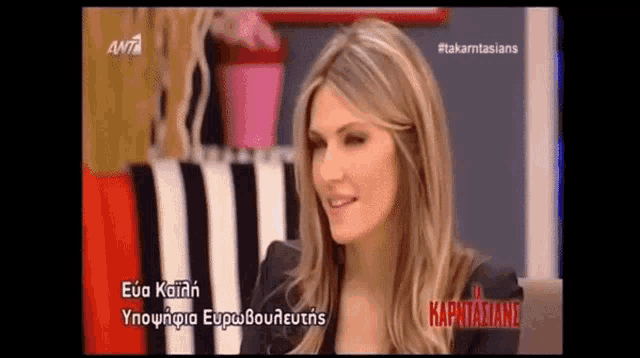 a woman in a black jacket is smiling on a television screen with greek writing on it .