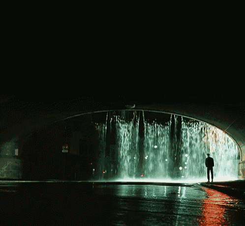 a man stands in front of a waterfall in a tunnel
