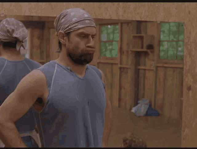 a man with a beard wearing a bandana looks at himself in a mirror