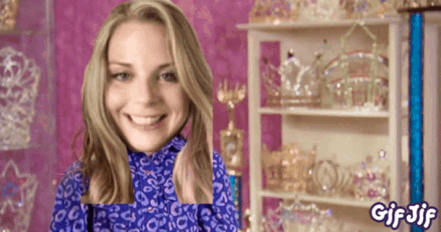 a woman in a blue leopard print shirt is smiling in front of a shelf full of tiaras and the words gif jif
