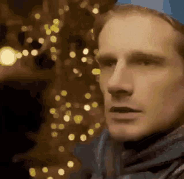 a man is standing in front of a christmas tree with lights .