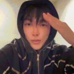 a person wearing a hoodie and headphones is saluting with their hand on their forehead .