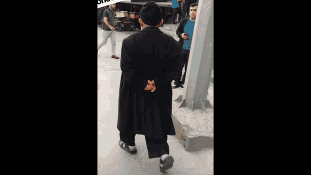 a man in a black coat stands in front of a sign that says ' oi ' on it
