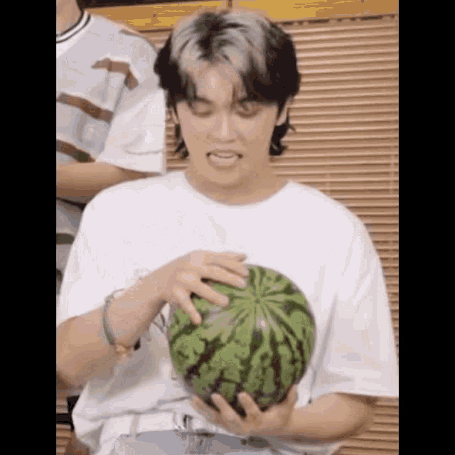 a young man is holding a watermelon in his hands and eating it .