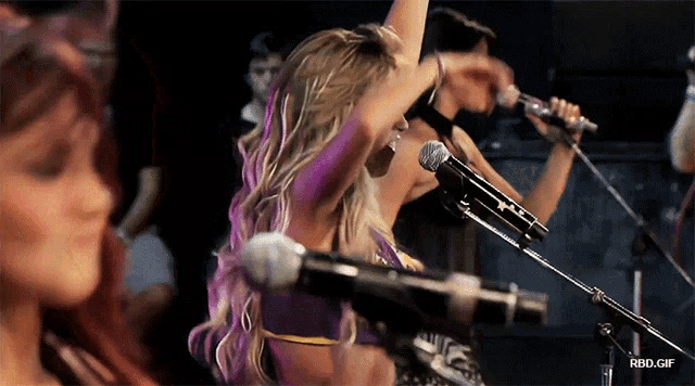 a woman with purple hair singing into a microphone with a rbd.gif below her