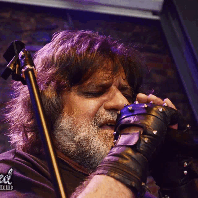 a man with a beard and spiked gloves sings into a microphone with a photo of him taken by reed studios