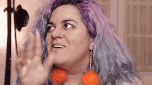 a woman with purple hair and orange earrings is smiling and making a funny face .