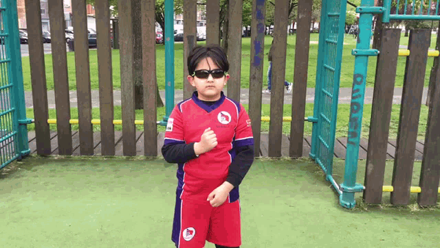 a young boy wearing sunglasses stands in front of a wooden fence that says rugby