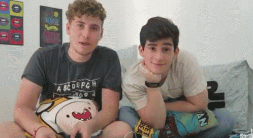 two young men are sitting on a couch and one of them is wearing a shirt that says abcdefghijklmn