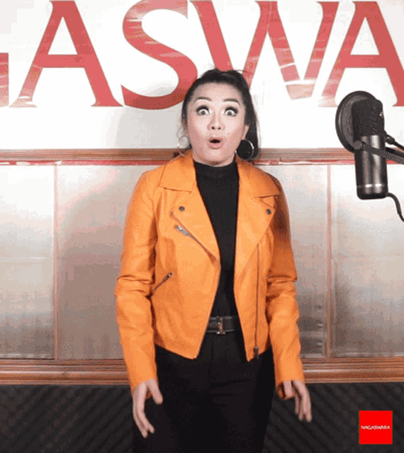 a woman in an orange jacket stands in front of a microphone in front of the word aswa