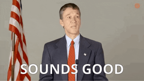 a man in a suit and tie is standing in front of an american flag with the words `` sounds good '' written below him .