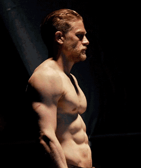 a shirtless man with a beard and red hair is standing in a dark room