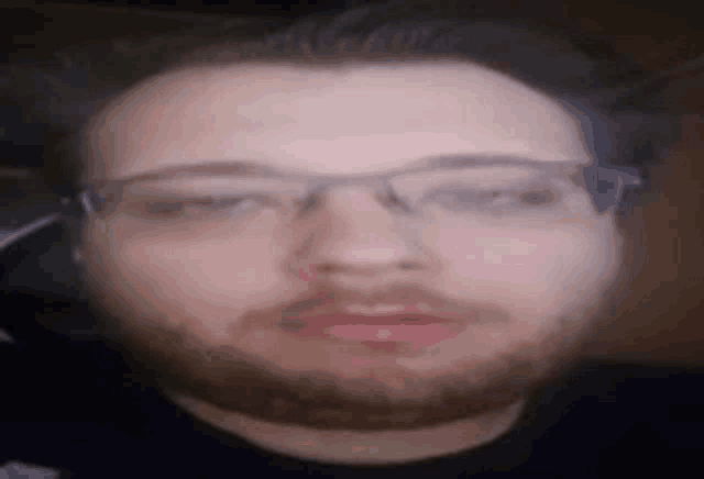 a man with a beard wearing glasses and a black shirt is looking at the camera .
