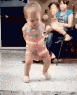 a little girl is dancing in a room while a woman holds another child