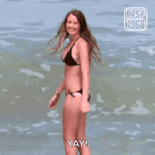 a woman in a bikini is standing in the ocean and says yay