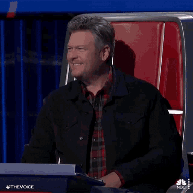 a man in a black jacket is smiling while sitting in a red chair
