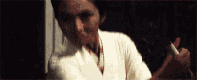 a woman in a white shirt is smoking a cigarette in a dark room .