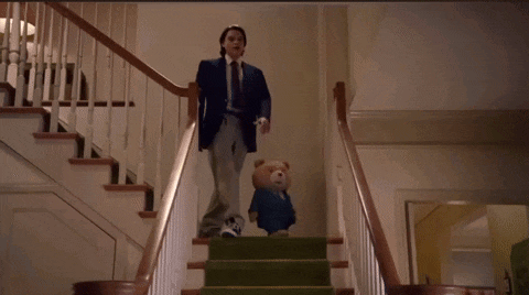 a man in a suit and tie is walking down stairs with a teddy bear
