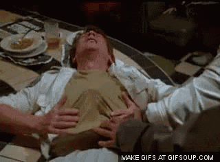 a man is laying on the floor with his hands on his stomach while another man holds his chest .
