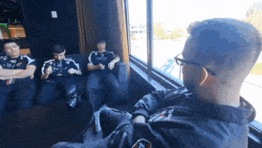 a group of men are sitting on a couch in front of a window talking to each other .