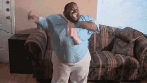 a man in a blue shirt and tie is dancing in front of a couch in a living room .
