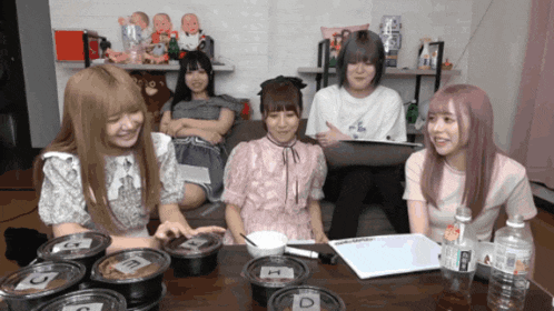 a group of girls are sitting around a table with bowls of food and a bottle of water with the letter e on it