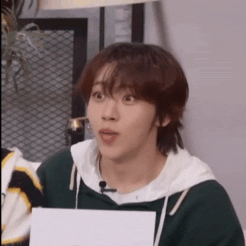 a young man is making a funny face while holding a piece of paper in his hand .
