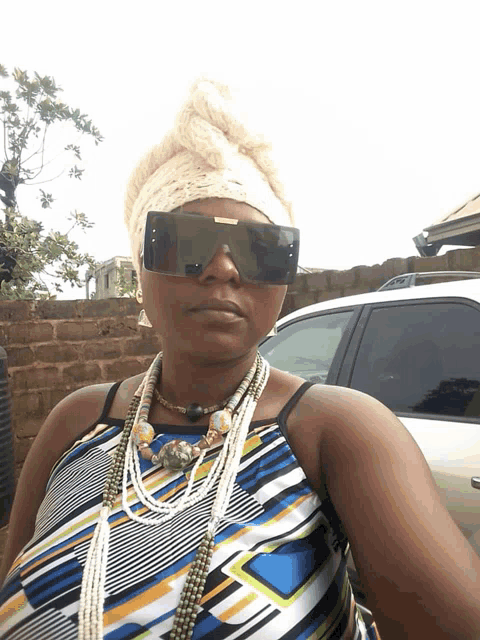 a woman wearing sunglasses and a necklace stands in front of a white suv