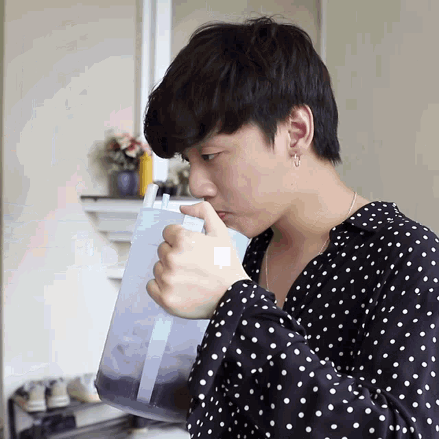 a man wearing a black and white polka dot shirt drinks from a pitcher