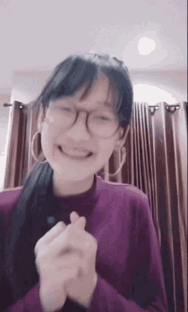 a young girl wearing glasses and a purple sweater is smiling