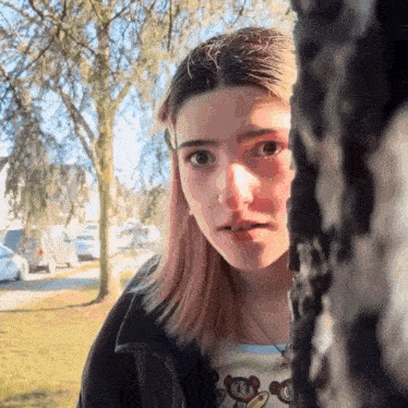 a girl looking out from behind a tree with a mickey mouse shirt on
