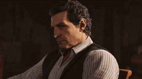 a man in a striped shirt and vest sits in a dark room