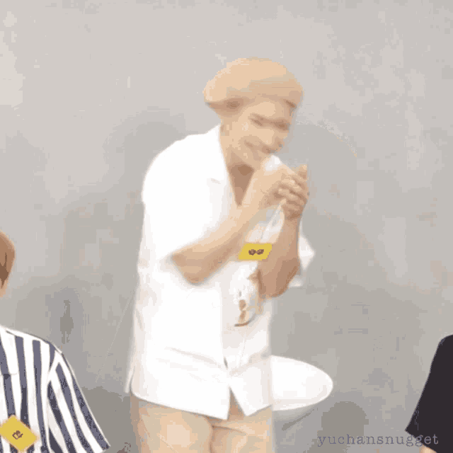 a man in a white shirt is standing in front of a toilet with a yellow tag that says yuchansnugget on it