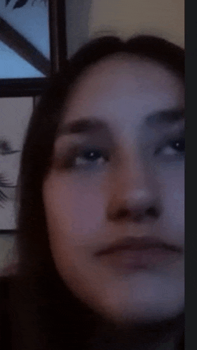 a close up of a woman 's face in a dark room with a picture in the background .