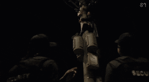 two security guards are standing next to a pole with buckets on it in the dark