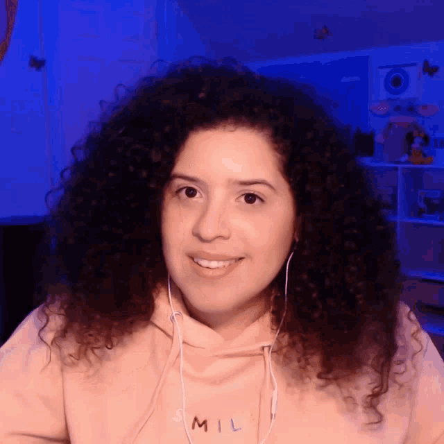 a woman with curly hair wears a pink hoodie that says smile