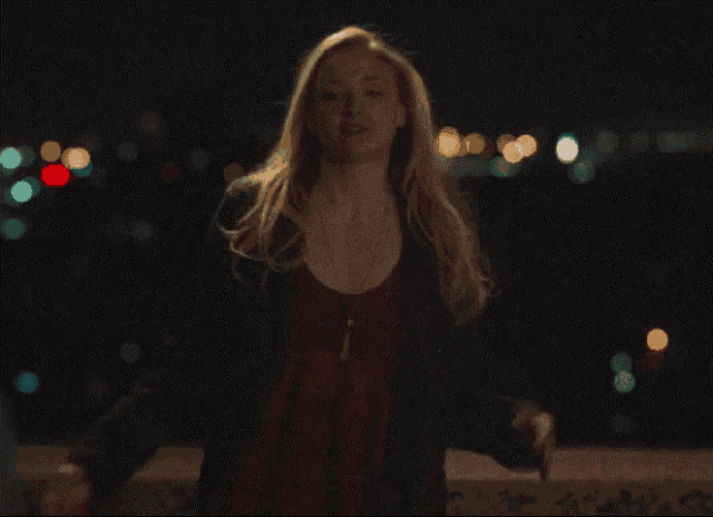 a woman in a black jacket stands in front of a blurry city skyline