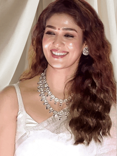 a woman wearing a silver necklace and earrings smiles for the camera