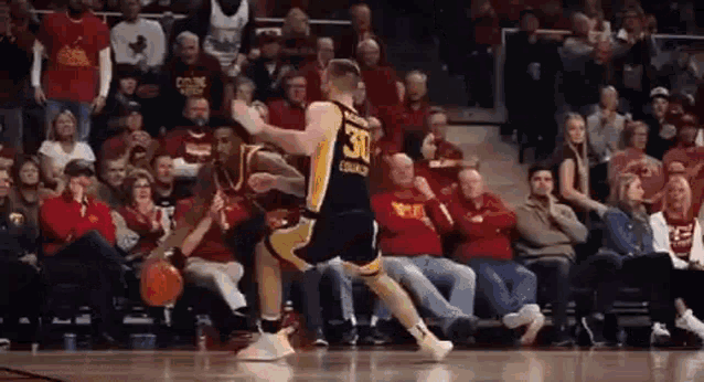 a basketball player wearing a jersey with the number 30 on it is dribbling a basketball in front of a crowd of people .