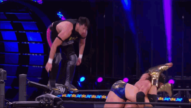 a wrestler is jumping over another wrestler in a ring while a referee watches