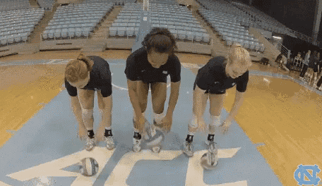 three female volleyball players on a court with the nc logo on the floor