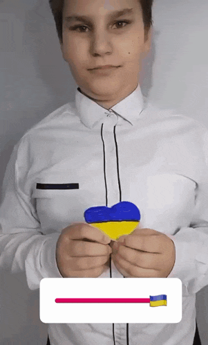 a boy in a white shirt is holding a blue and yellow heart in his hands