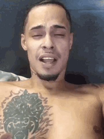 a shirtless man with a tattoo on his chest is making a funny face with his eyes closed .