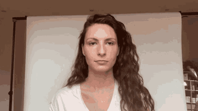 a woman with long curly hair is standing in front of a white board .